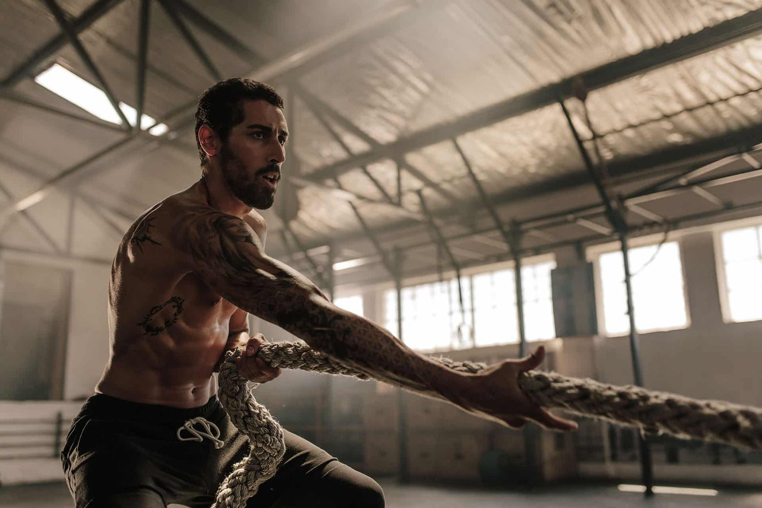 Fit male pulling battle rope in warehouse gym