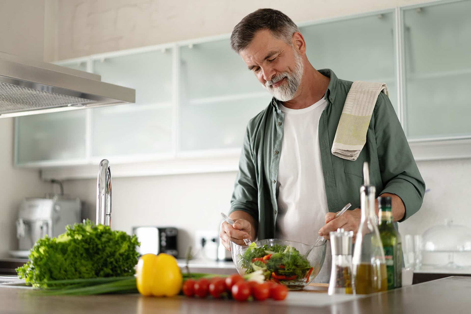 Senior male mixing salad in kitchen